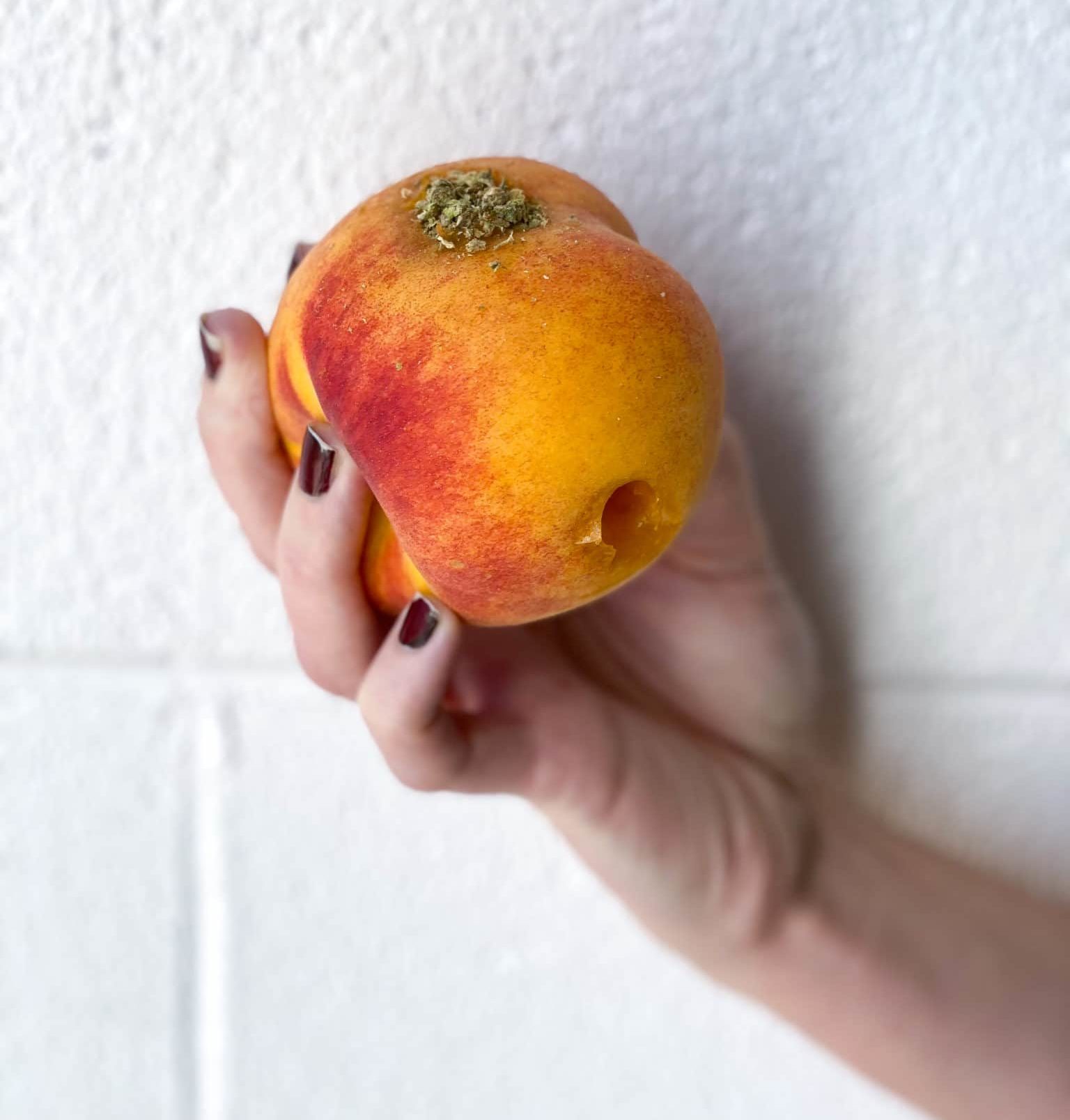 hand holding a DIY peach pipe with cannabis flower