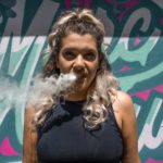 woman standing in front of a painted wall exhaling smoke