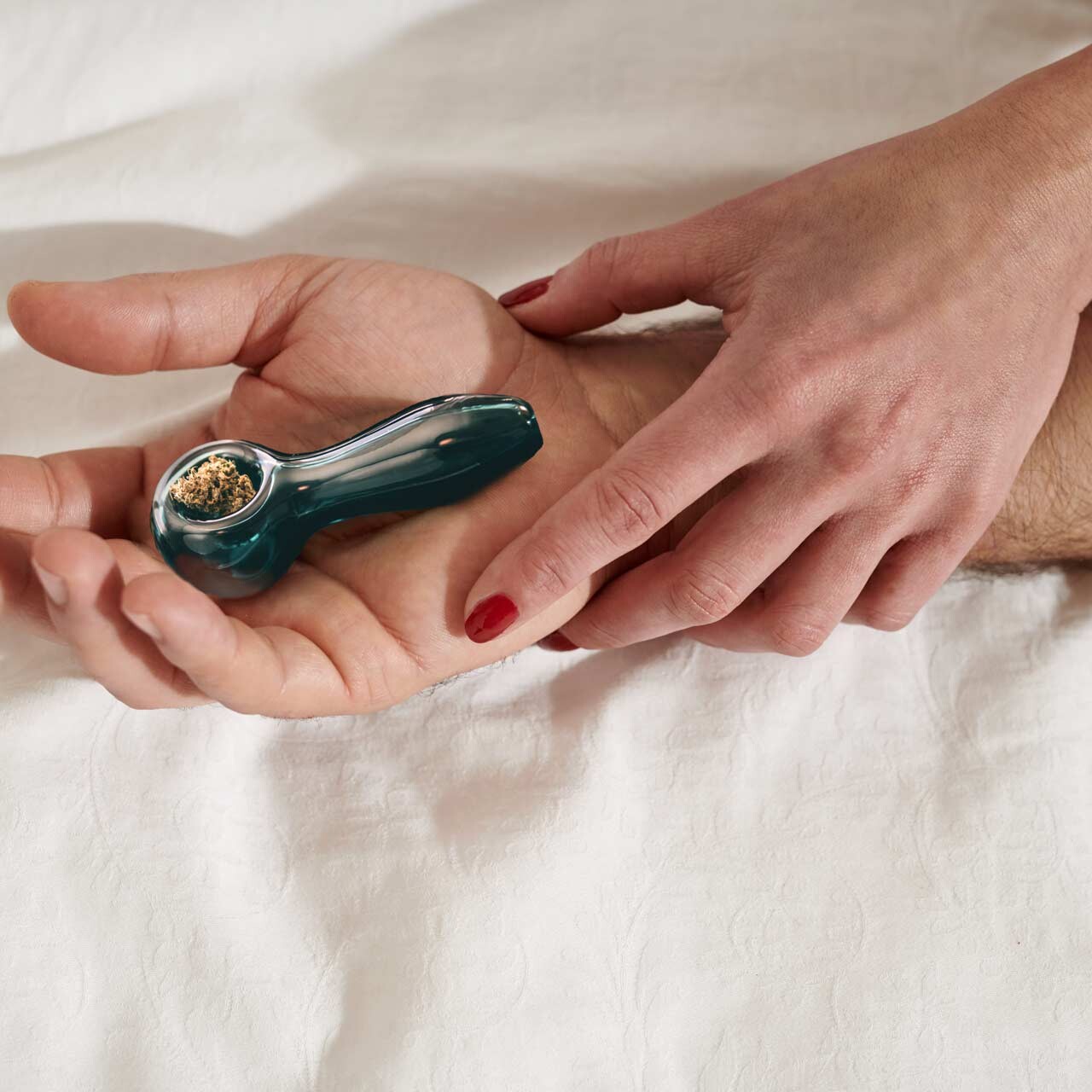 couple holding glass cannabis pipe in bed