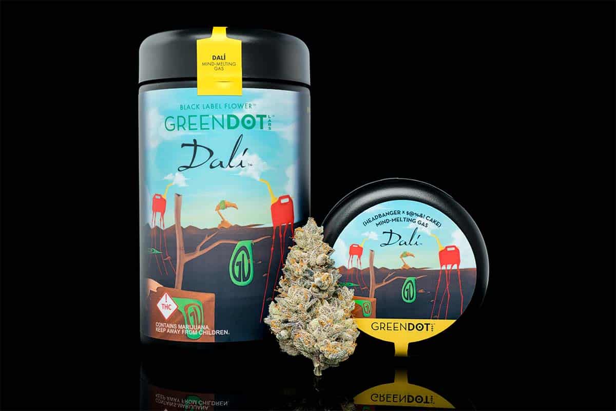 Green Dot Labs Black Label Flower 'Dali' cannabis product packaging displayed alongside a dense cannabis bud, featuring surrealist-inspired artwork and a reflective black background.